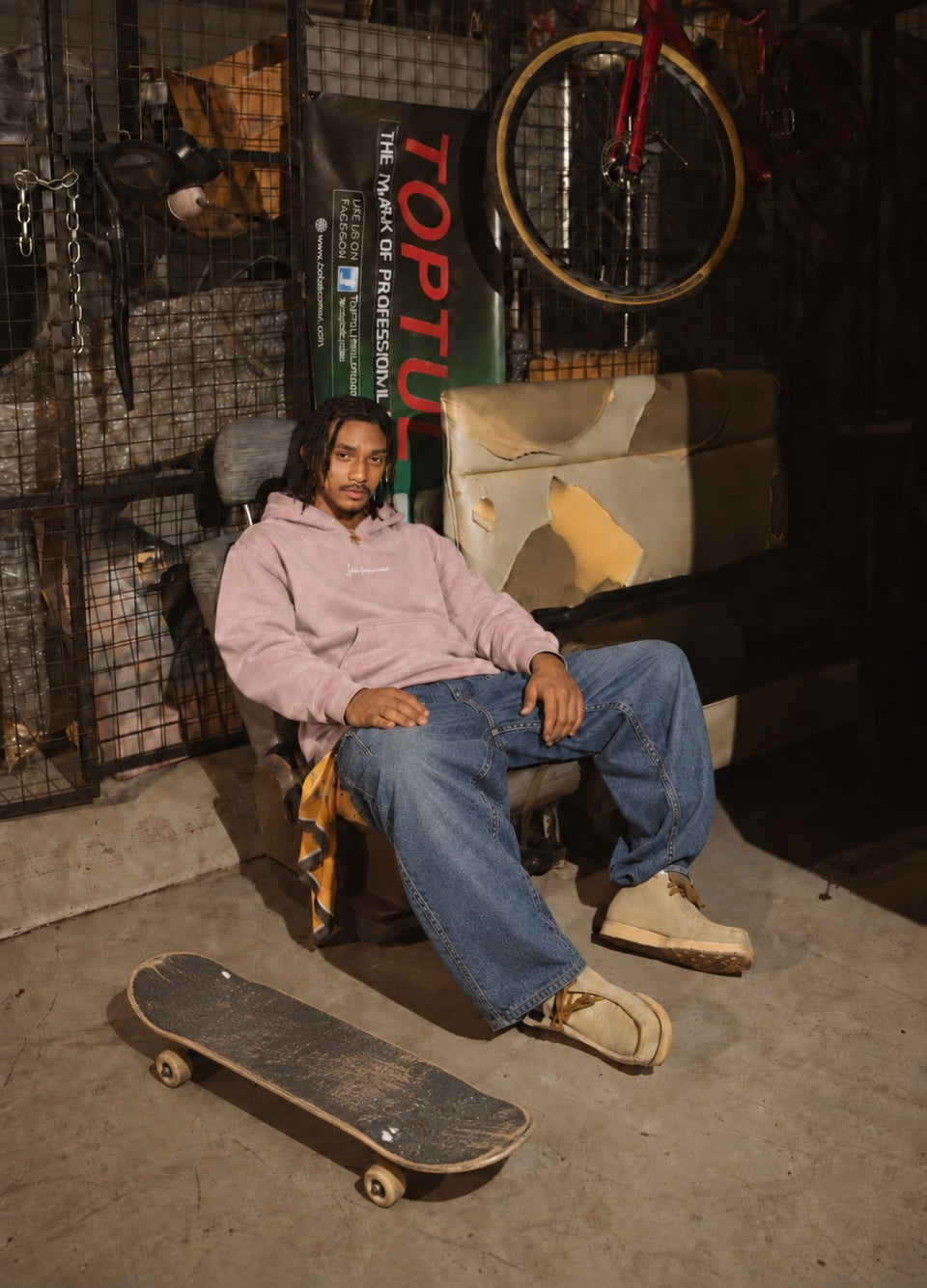 Ragazzo con jeans larghi seduto in un garage, skateboard ai piedi